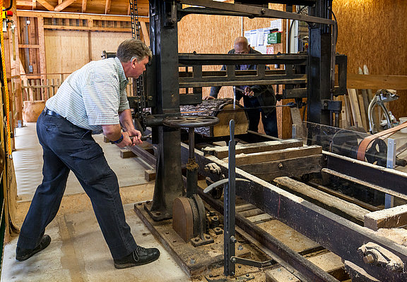 Das Bild zeigt einen Mann, der im Drechselraum des Hunsrücker Holzmuseum eine alte Maschine bedient im Rahmen einer Gästeführung.