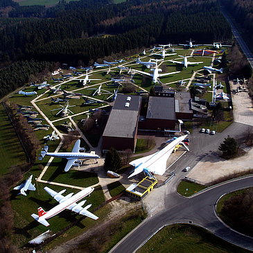 Das Bild zeigt eine Luftaufnahme vom Gelände der Flugausstellung Junior mit zahlreichen Flugzeugen und dem Hauptgebäude.