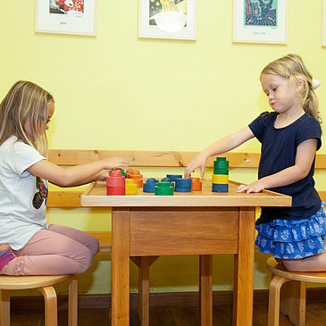 Das Bild zeigt zwei Mädchen die an einem Spieltisch im Spielzimmer des Hunsrücker Holzmuseums sitzen und mit Bausteinen spielen.